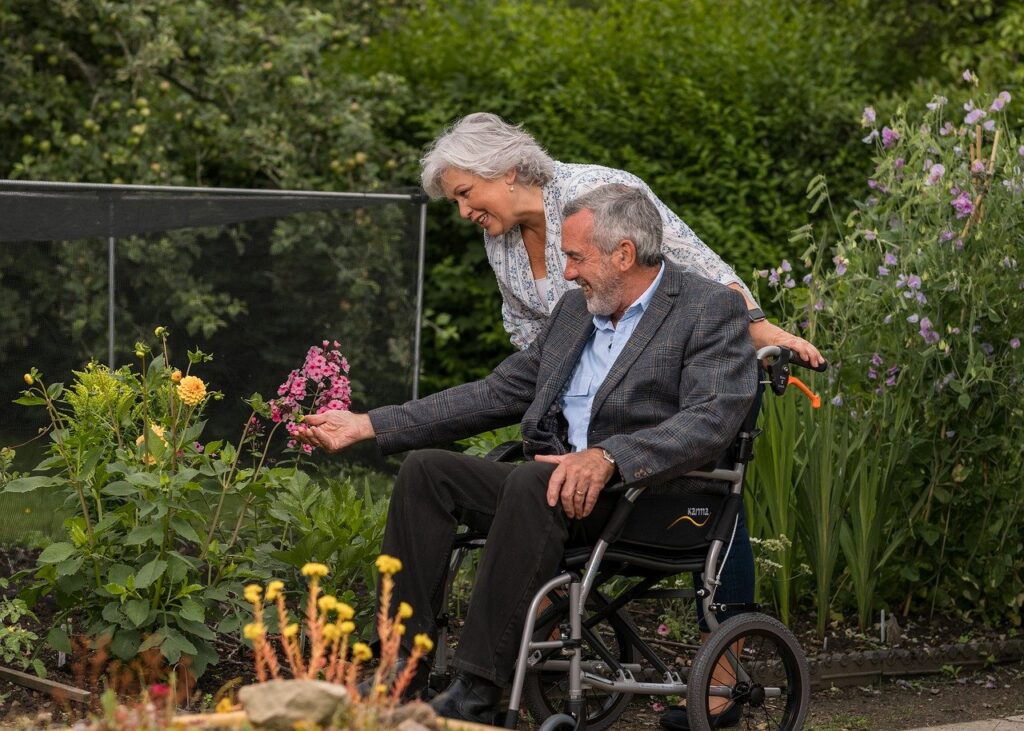 coppia di anziani - lui in sedia rotelle - visita di un giardino